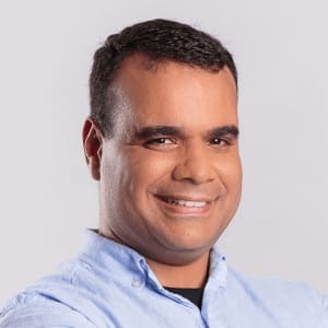 smiling man in a light blue shirt against a neutral background, professional portrait with a friendly demeanor