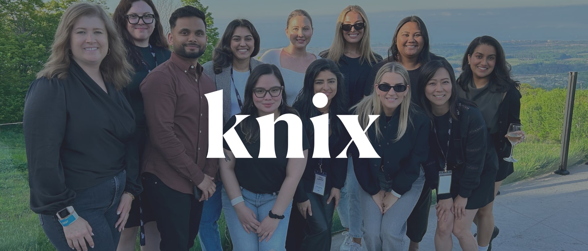 diverse group of people smiling outdoors with scenic background, branding 'knix' in foreground, outdoor team gathering celebrating knix