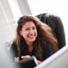smiling woman with long curly hair in a modern office, confident professional in a black shirt sitting at a desk