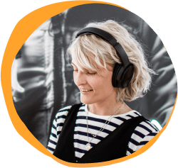 woman with headphones smiling, striped shirt and short blonde hair against a vibrant background