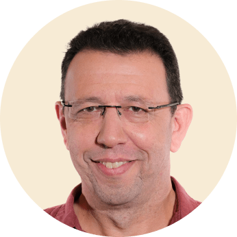 smiling man with glasses in a circular frame, casual portrait with neutral background and warm expression