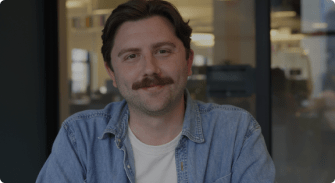man with a mustache in a light blue denim jacket, modern office setting with blurred background elements