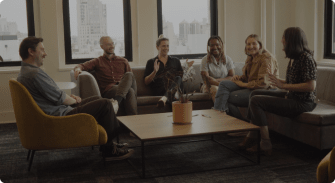 casual group discussion in modern office overlooking city, diverse team sitting on sofas with plants and natural light