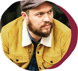 man with beard in mustard jacket and gray cap, close-up portrait in outdoor setting with warm color tones